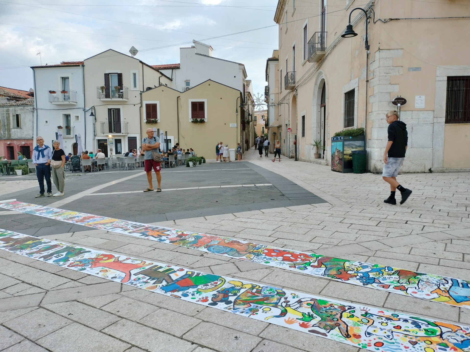 Termoli, piazza con persone in cammino, e strisce di disegni colorati sul selciato.
