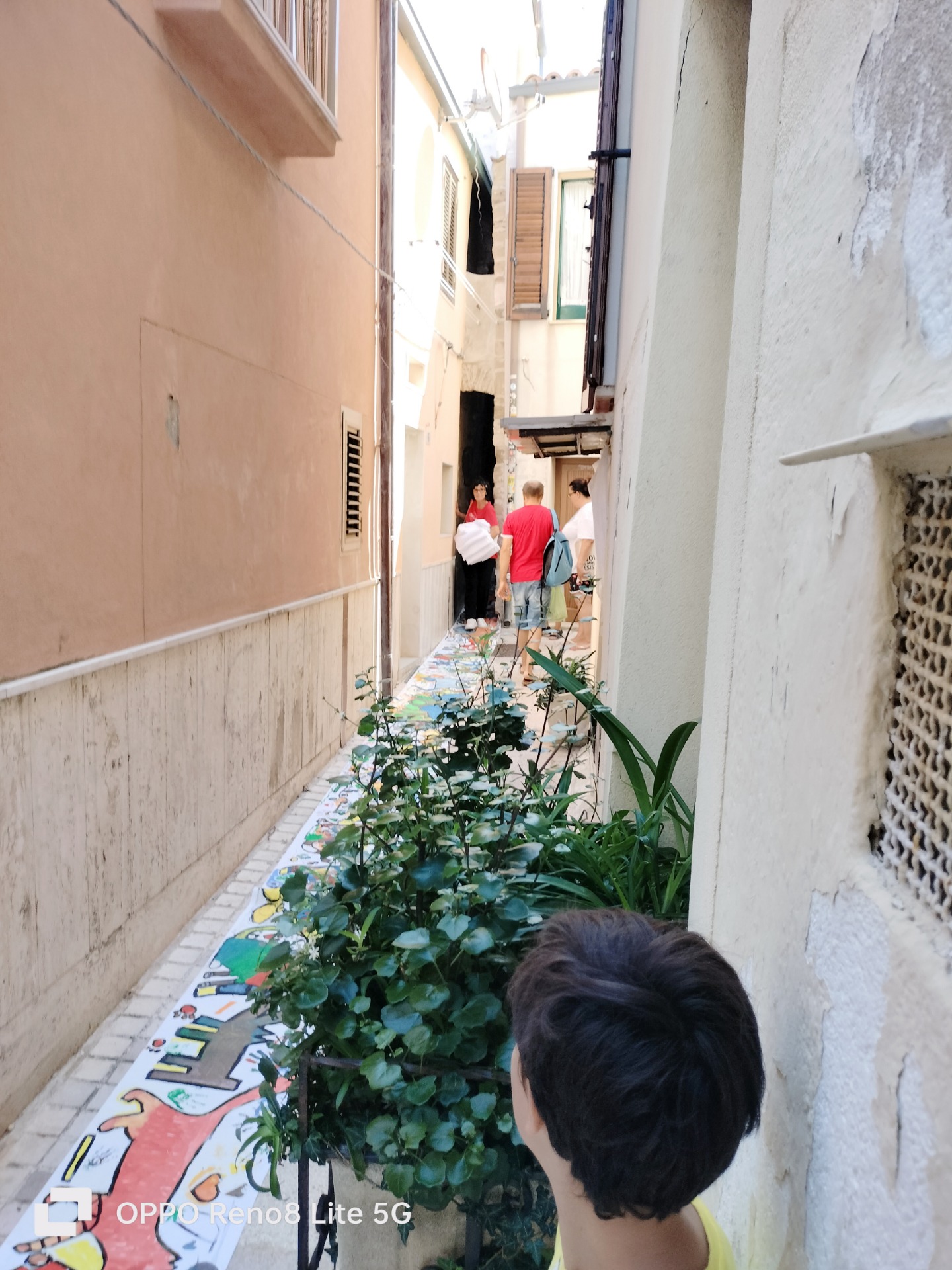 Vicolo stretto con persone che camminano sopra la tela decorata.