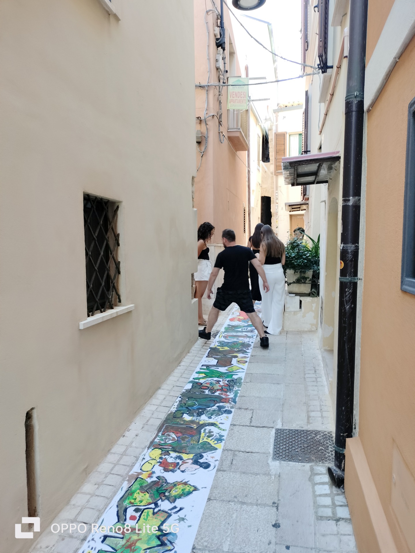 Vicolo stretto di Termoli con persone che camminano evitando di calpestare la striscia colorata.