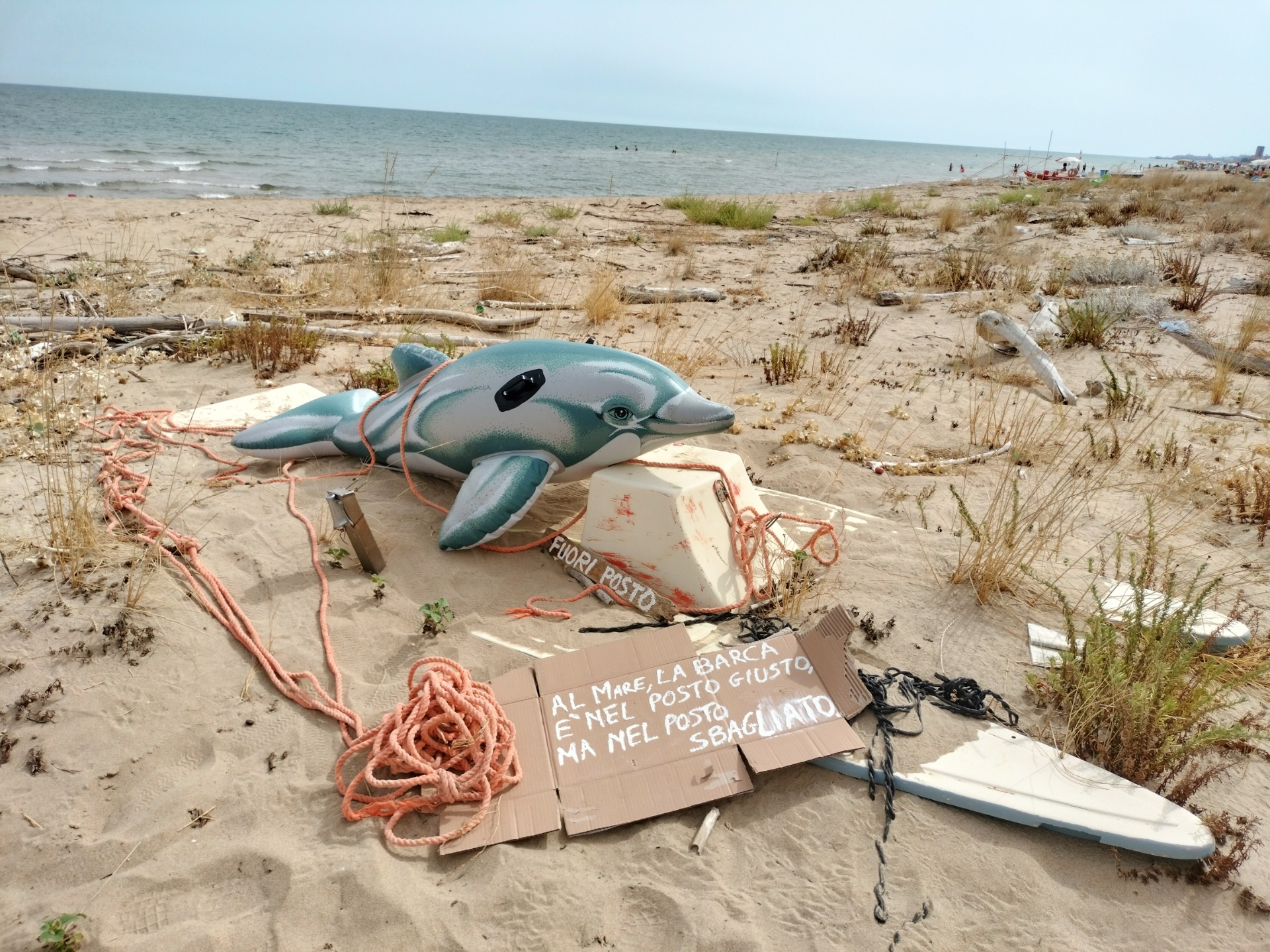 Il delfino gonfiabile dei Fratellini Margiotta su una barca insabbiata sulla spiaggia, accanto al cartello dell’installazione Fuori Posto.