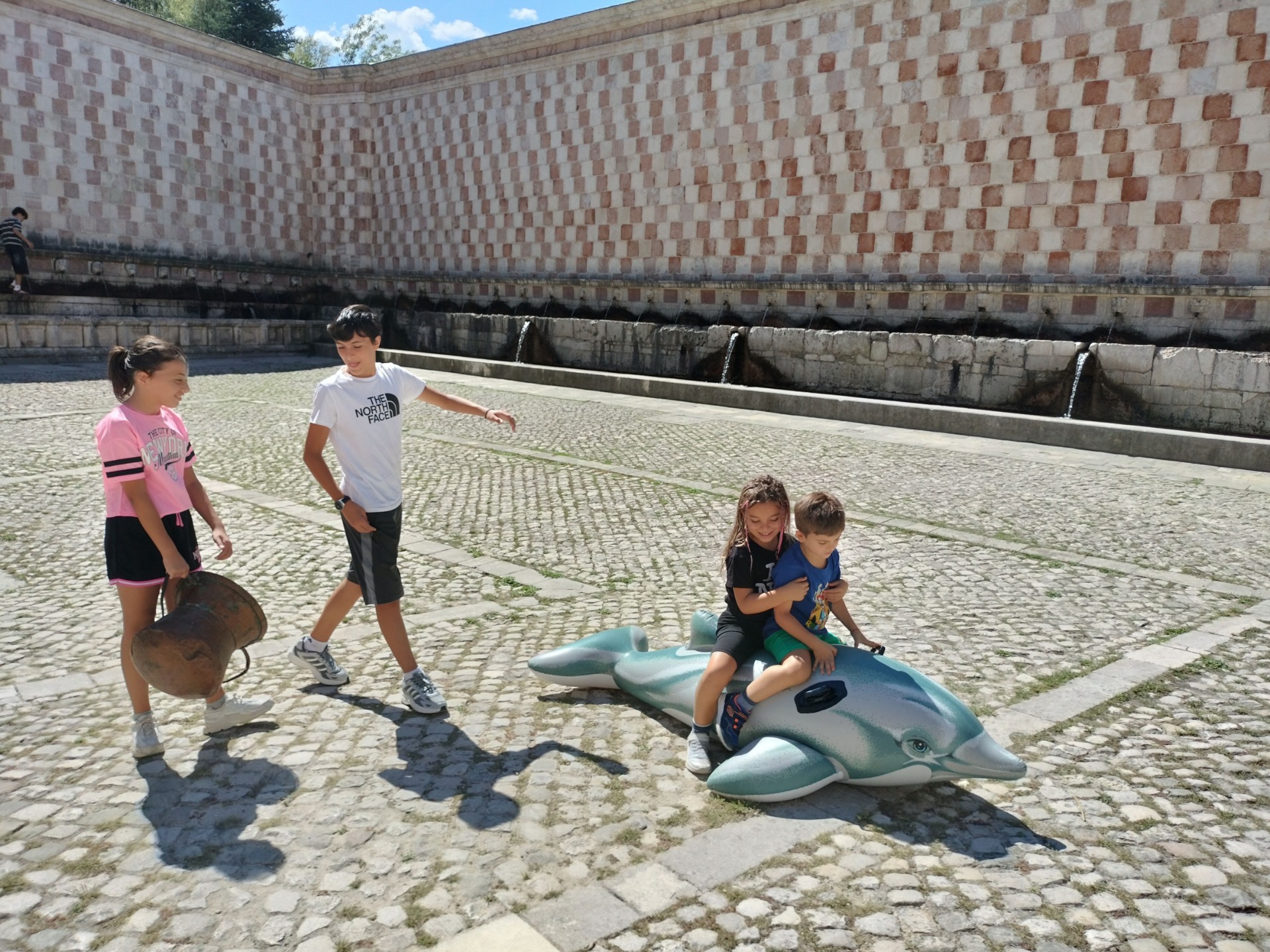due bambini calacano il delfino al centro della piazza della fontana delle 99 cannelle L' Aquila.
