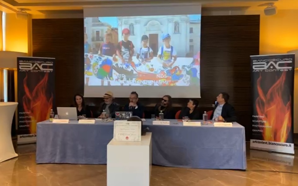 Montecarlo Tavolo di conferenza con relatori seduti davanti a schermo, per premiare i Fratellini Margiotta e gli altri bambini con il premio della critica.