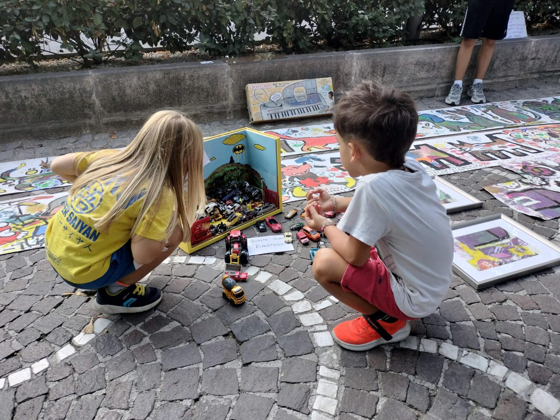 Due bambini seduti su pavimento che vedono il diorama creato con le vecchie macchinine.